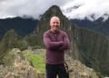 Don Trynor standing on a lookout during his Machu Picchu science travel experience, with the ancient citadel behind him and surrounded by steep mountain cliffs and drifting clouds.