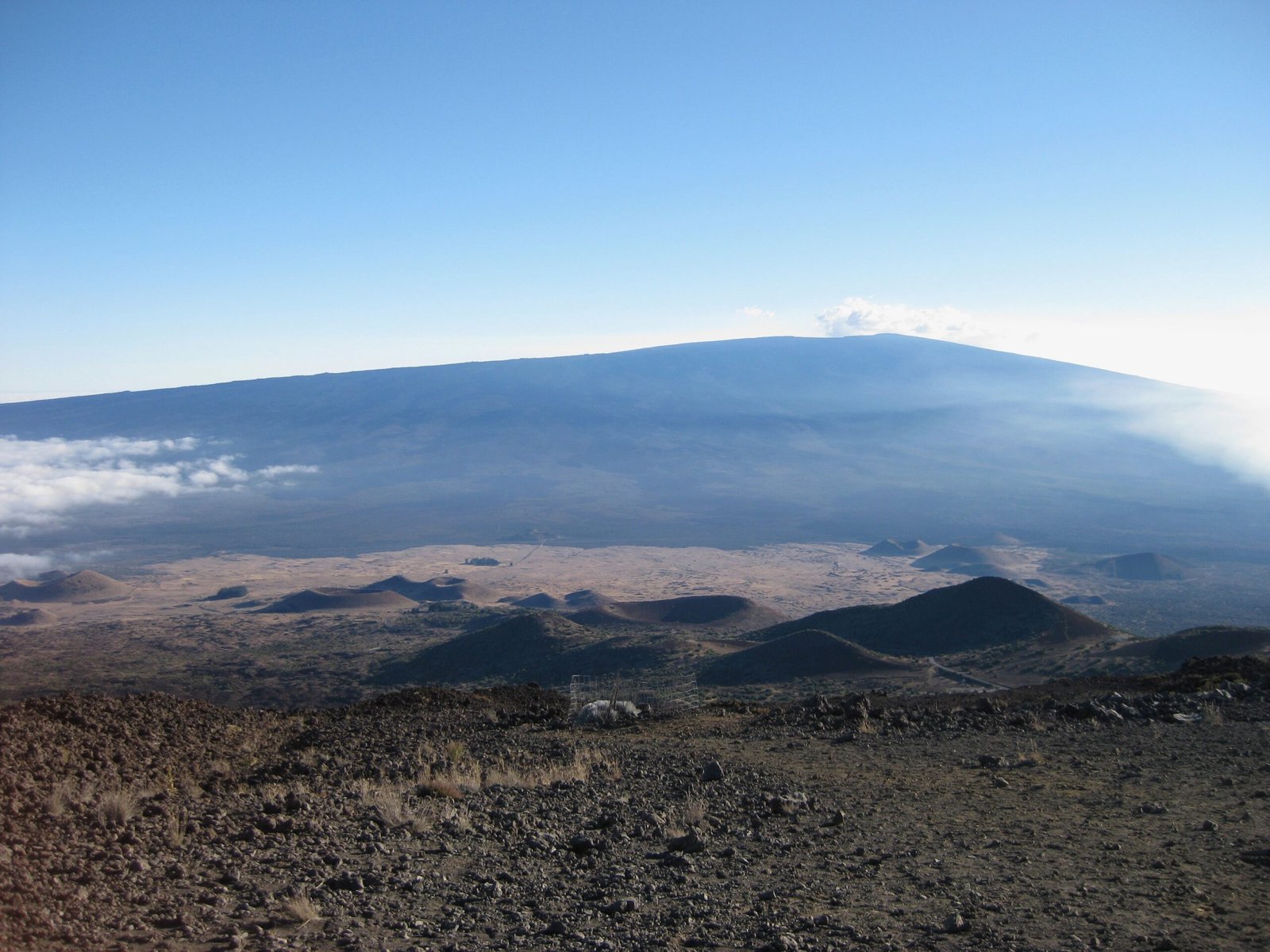 View from Mauna Kea’s slope showing Mauna Loa in the distance, with clouds filling the valley between the two volcanic peaks.