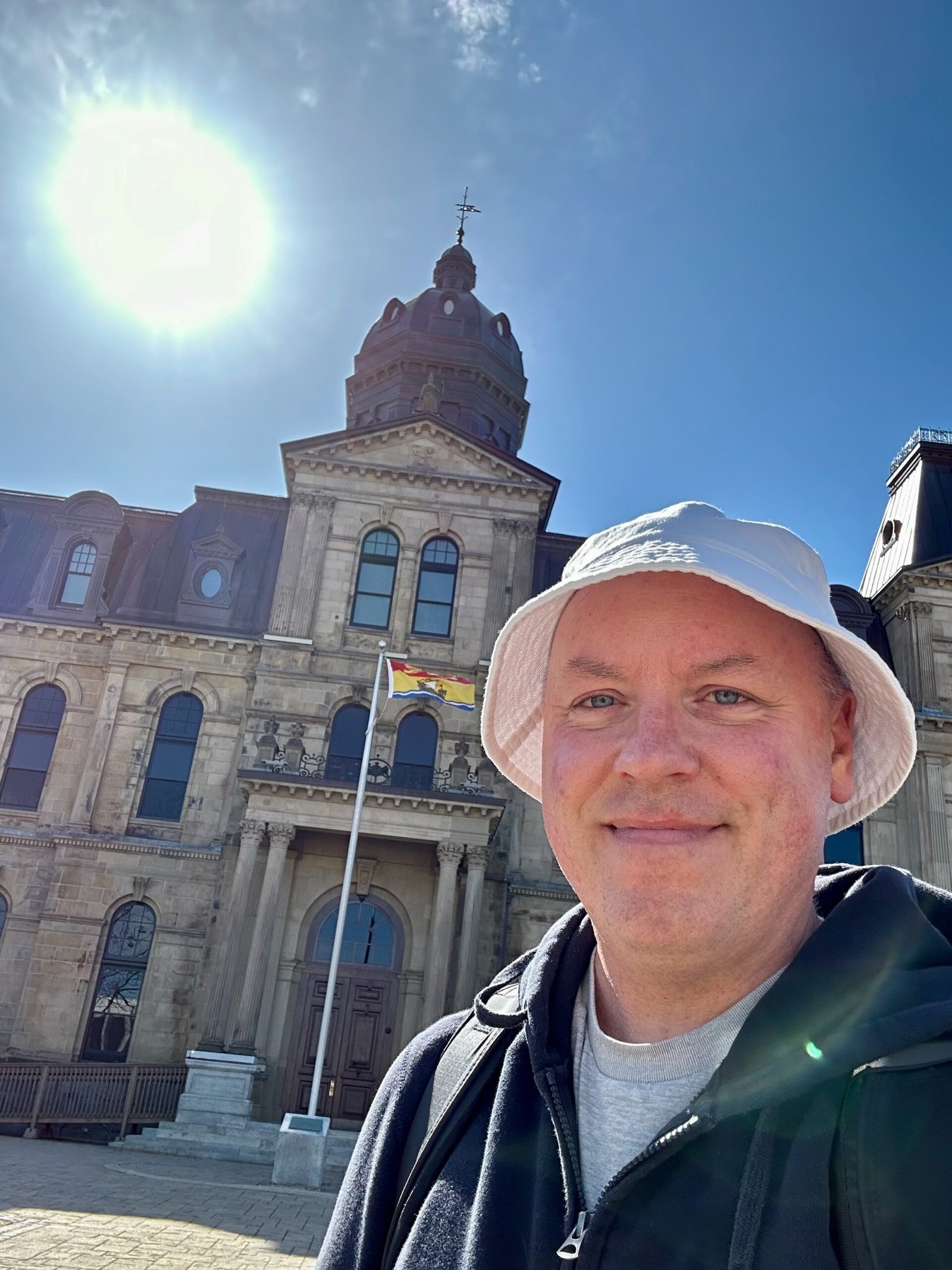 Don Trynor, author of Curious Don, standing in front of the Legislative Assembly of New Brunswick in Fredericton, smiling in anticipation of witnessing his first total solar eclipse on April 8, 2024.