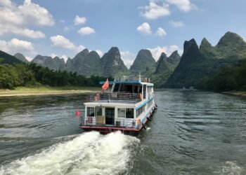 A river cruise boat on Li River China in Guilin, with towering limestone peaks rising against a bright sky.