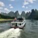 A river cruise boat on Li River China in Guilin, with towering limestone peaks rising against a bright sky.