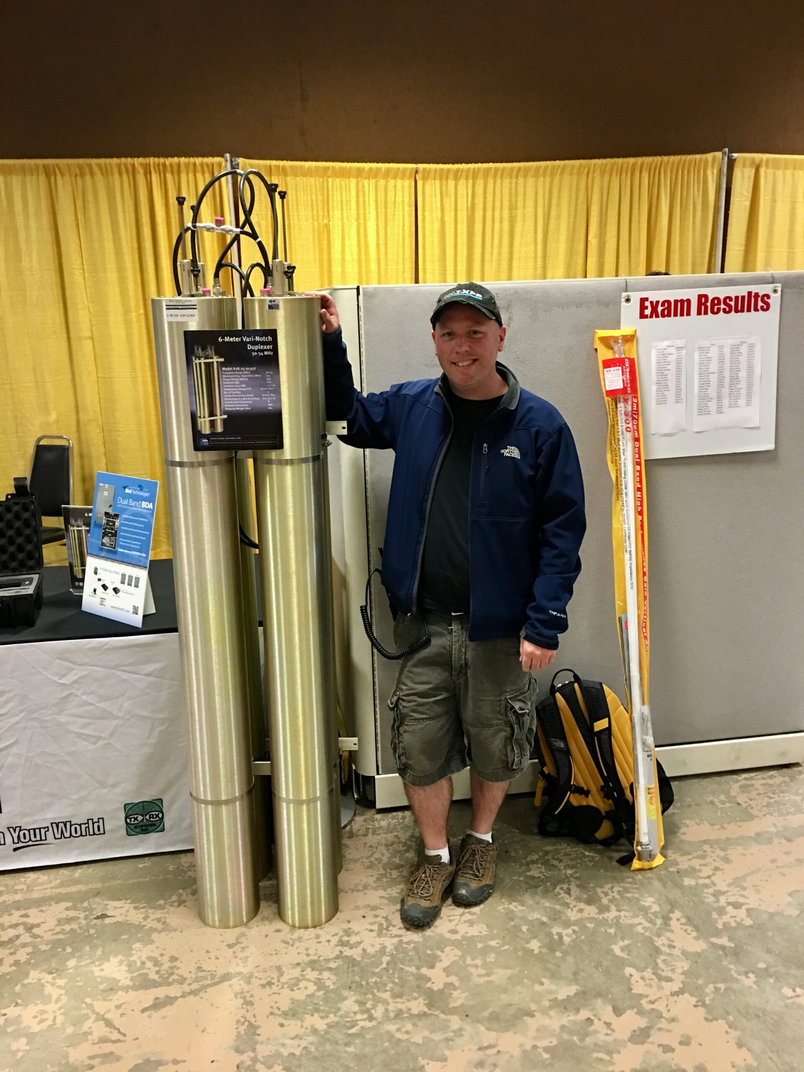 Don Trynor, author of Curious Don, standing beside a piece of amateur radio equipment at Dayton Hamvention, surrounded by event displays.