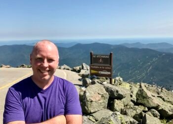 Don Trynor at the summit of Mount Washington, with the Auto Road on the left and panoramic White Mountain views in the background.