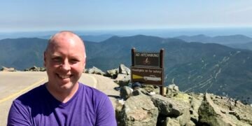 Don Trynor at the summit of Mount Washington, with the Auto Road on the left and panoramic White Mountain views in the background.