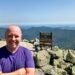 Don Trynor at the summit of Mount Washington, with the Auto Road on the left and panoramic White Mountain views in the background.