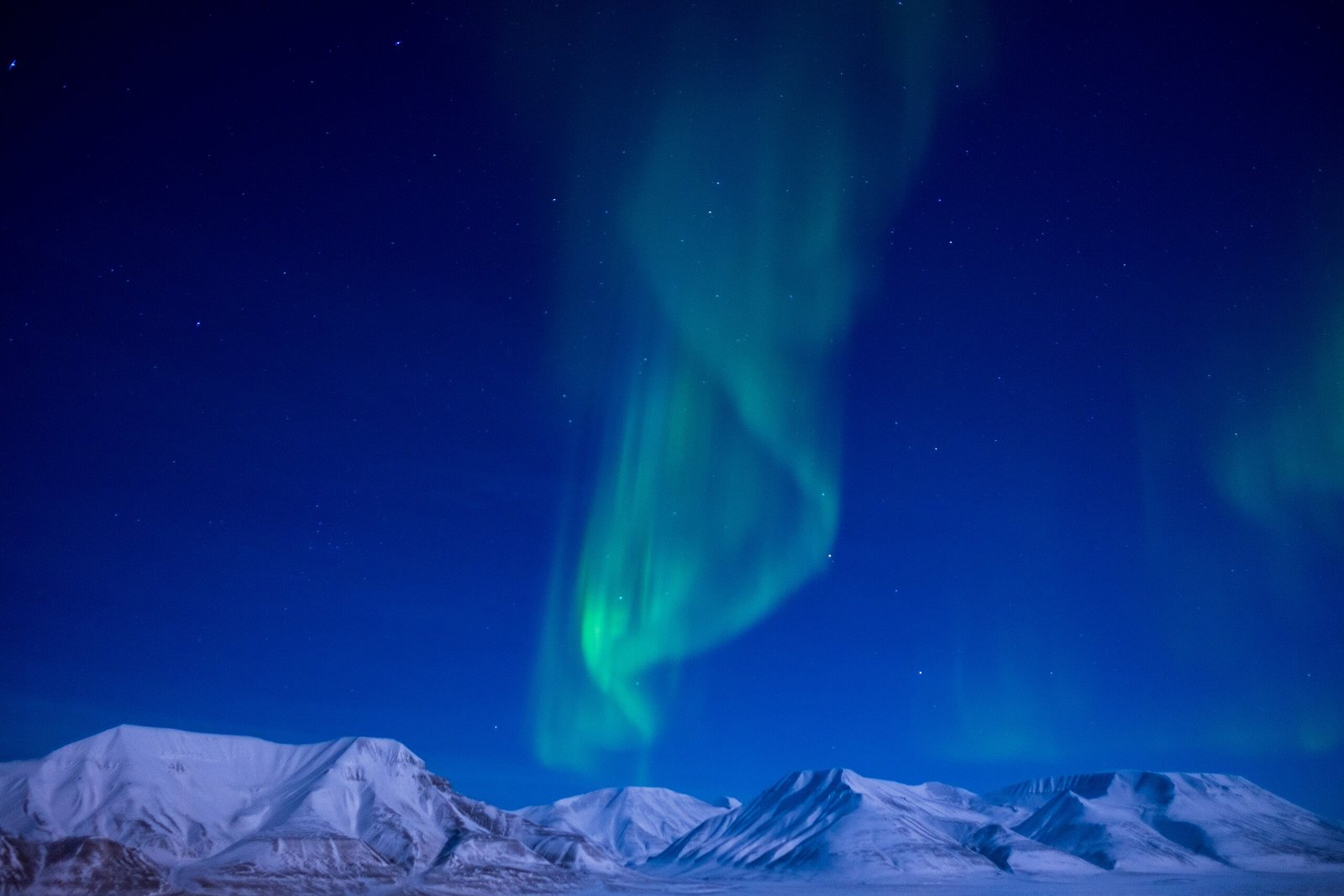 he Northern Lights glowing in vibrant green and purple hues over the snowy Arctic landscape of Svalbard, Norway. Photo by Frode Ramone, via Wikimedia Commons.