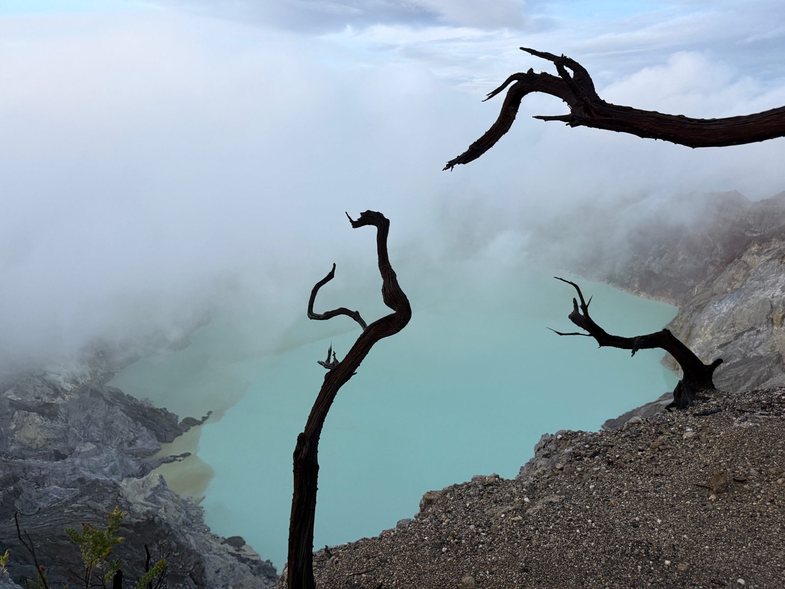 Turquoise crater lake of Kawah Ijen volcano in East Java, Indonesia, at dawn with mist and toxic sulfur clouds rising.