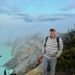 Don Trynor, author at Curious Don, stands on the rim of the Kawah Ijen volcano crater in Indonesia, with a turquoise crater lake visible below.