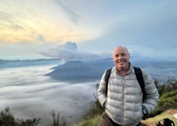 Don Trynor standing at Bukit Cinta at dawn, with the smoking Mount Bromo volcano rising above a mist-filled Tengger Caldera in the background.