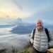 Don Trynor standing at Bukit Cinta at dawn, with the smoking Mount Bromo volcano rising above a mist-filled Tengger Caldera in the background.