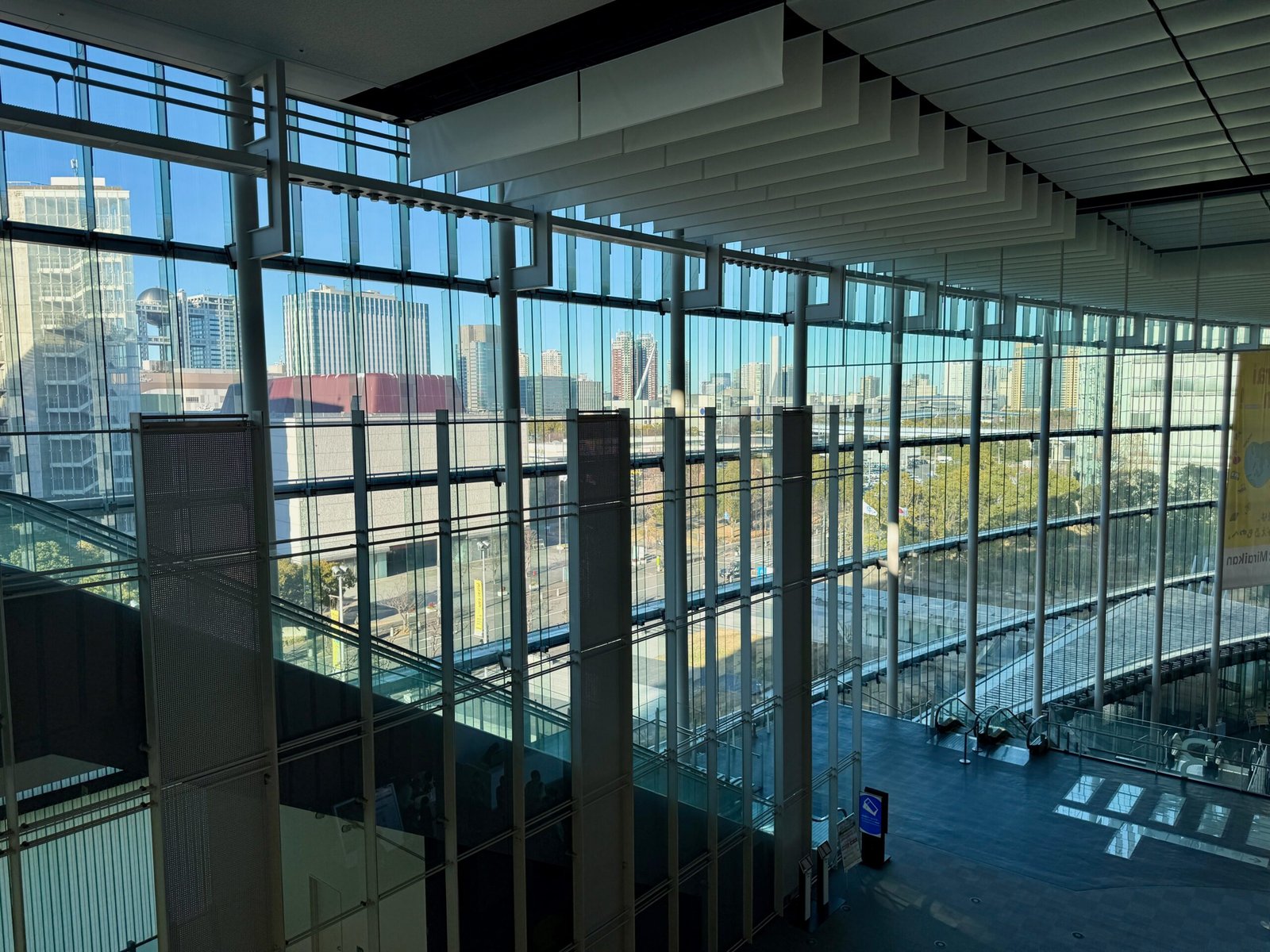 Glass atrium at Miraikan in Tokyo with views of the modern Odaiba skyline through tall windows.