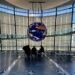 Silhouetted visitors sitting at a table in front of the illuminated Geo-Cosmos globe in Miraikan’s main hall.