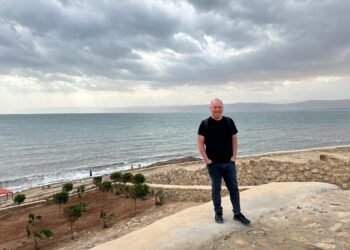 Don Trynor, author of the Curious Don website, standing in front of the Dead Sea in Jordan, with the west bank of the Dead Sea in Israel in the background.