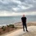 Don Trynor, author of the Curious Don website, standing in front of the Dead Sea in Jordan, with the west bank of the Dead Sea in Israel in the background.