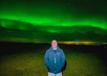 Don Trynor, author of the Curious Don website, poses beneath the vibrant green aurora borealis in Iceland during a February trip. The northern lights shine brilliantly overhead, illuminating the night sky.