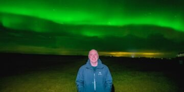 Don Trynor, author of the Curious Don website, poses beneath the vibrant green aurora borealis in Iceland during a February trip. The northern lights shine brilliantly overhead, illuminating the night sky.