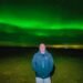 Don Trynor, author of the Curious Don website, poses beneath the vibrant green aurora borealis in Iceland during a February trip. The northern lights shine brilliantly overhead, illuminating the night sky.