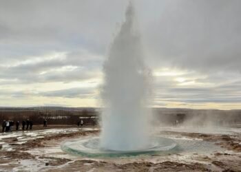 The Strokkur Geyser erupting in Iceland, with boiling water shooting into the air and steam rising around it.