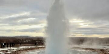 The Strokkur Geyser erupting in Iceland, with boiling water shooting into the air and steam rising around it.