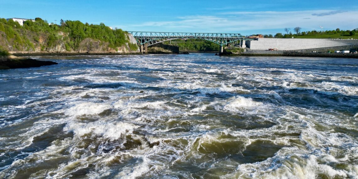 Turbulent whitewater rapids at the Reversing Falls in Saint John, New Brunswick, viewed at low tide with the Reversing Falls Bridge spanning the gorge in the background.