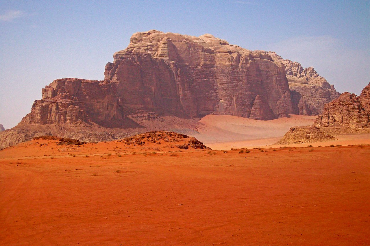 Wadi Rum desert with red sand and a distant red mountain, resembling Mars—one of the top places that look like Mars on Earth.