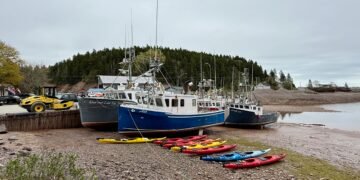 Fishing boats and kayaks rest on the exposed seafloor during a Bay of Fundy tide in St. Martins, New Brunswick, showcasing the region’s extreme tidal range.