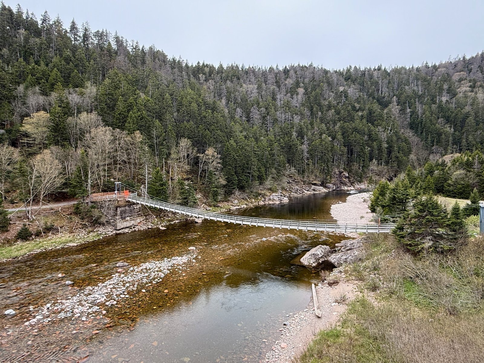 Suspension bridge over the Salmon River with evergreen forest and glacial erratics in the riverbed