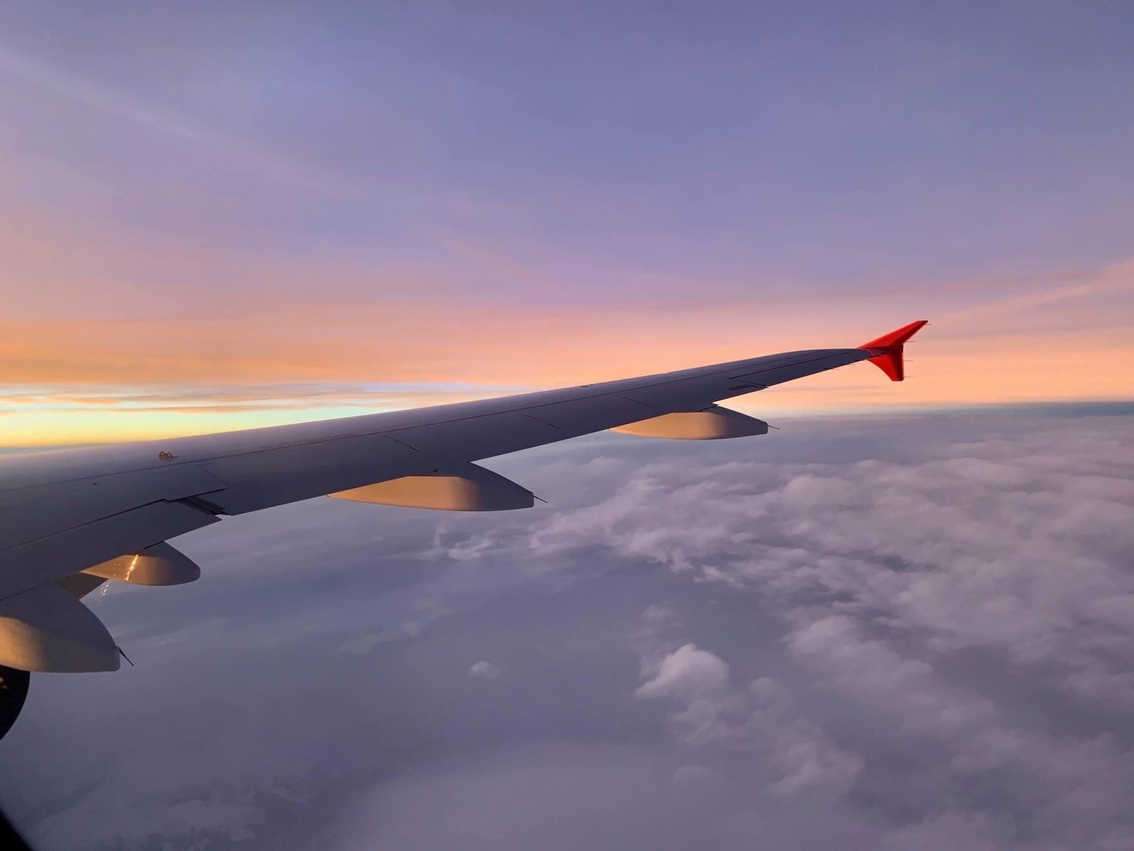 Airplane wing at sunset with clouds above and below—illustrating how flying becomes one of the places where time slows down or speeds up.