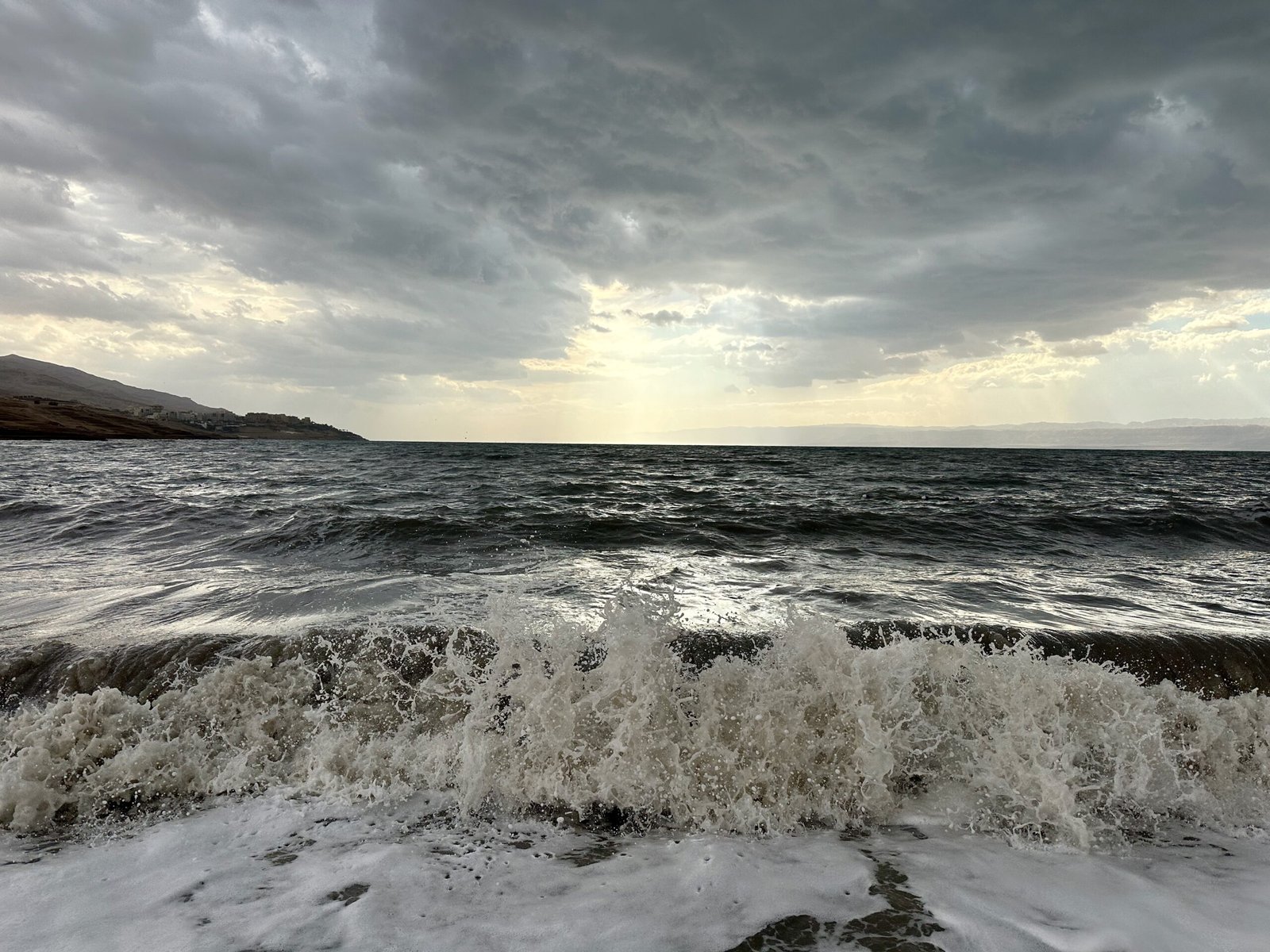 Waves crashing on the Jordanian shore of the Dead Sea under sun rays, illustrating one of the places where time slows down.