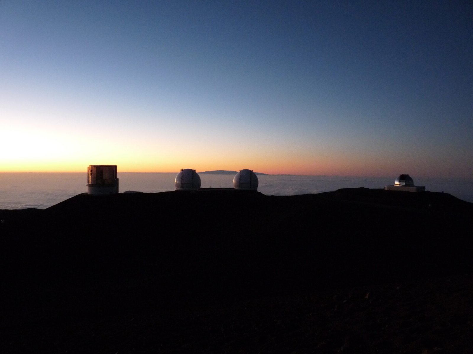 Mauna Kea astronomical observatories at sunset, with a sea of clouds below—one of the places where time slows down.