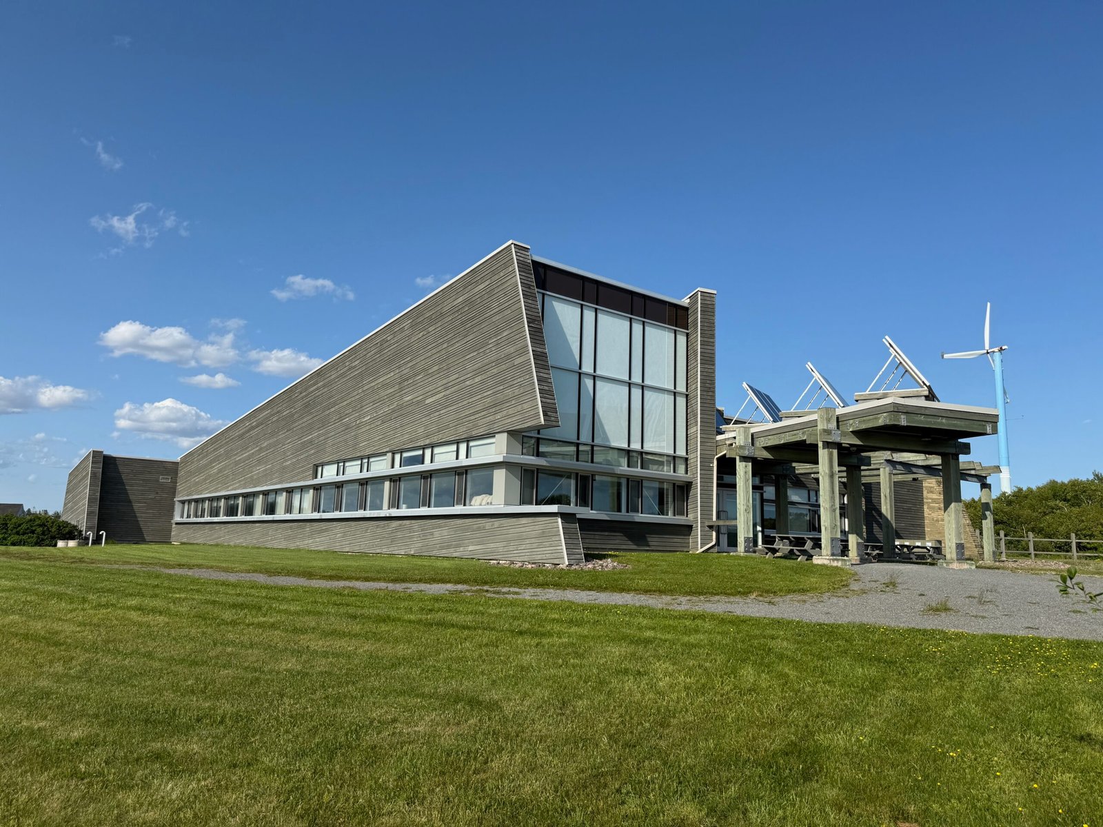 Modern building of the Joggins Fossil Cliffs visitor centre and museum with large windows, solar panels, and a wind turbine, set against a blue sky.