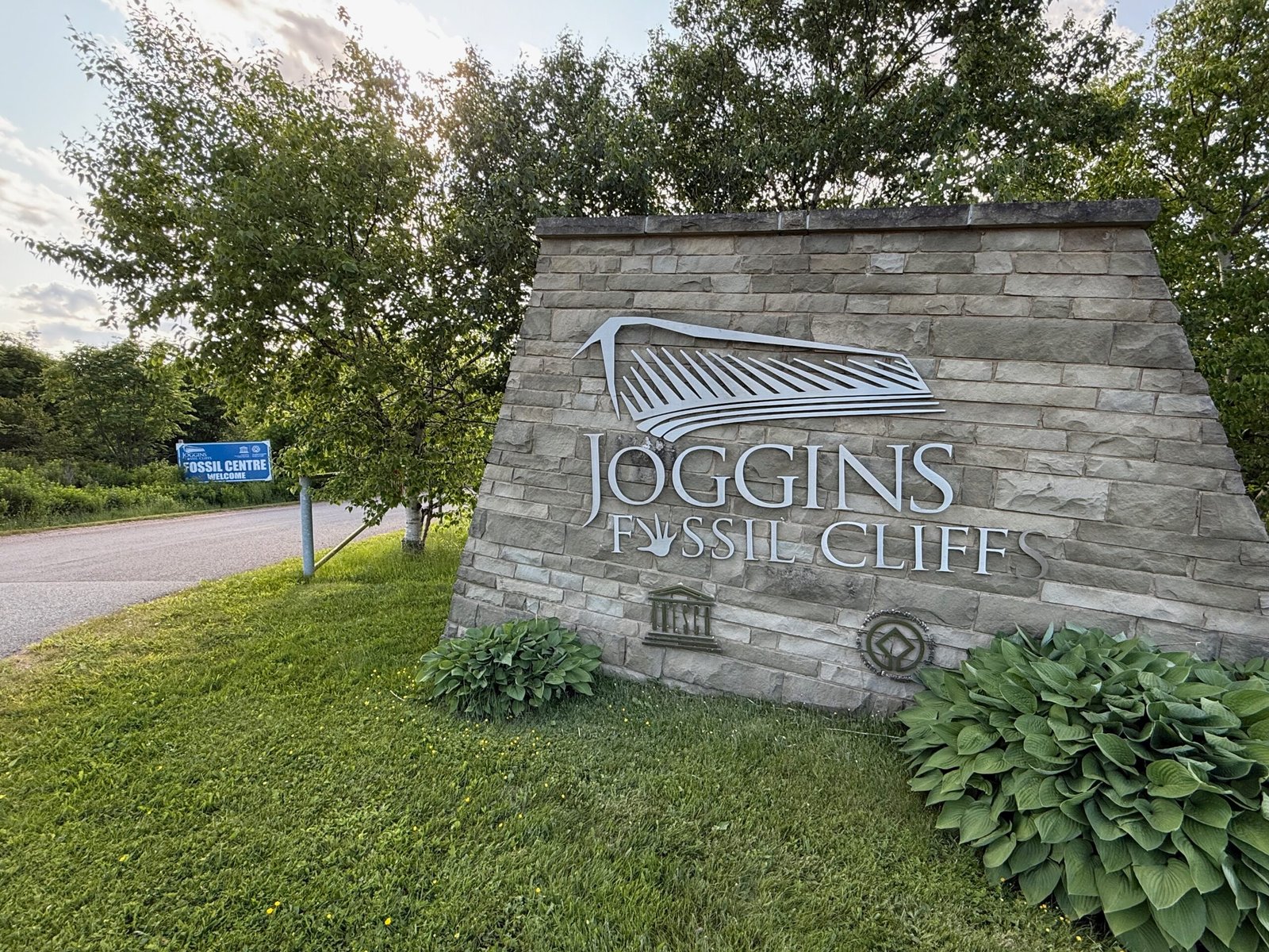 Entrance sign for Joggins Fossil Cliffs UNESCO World Heritage Site with cliffs and sky in the background.