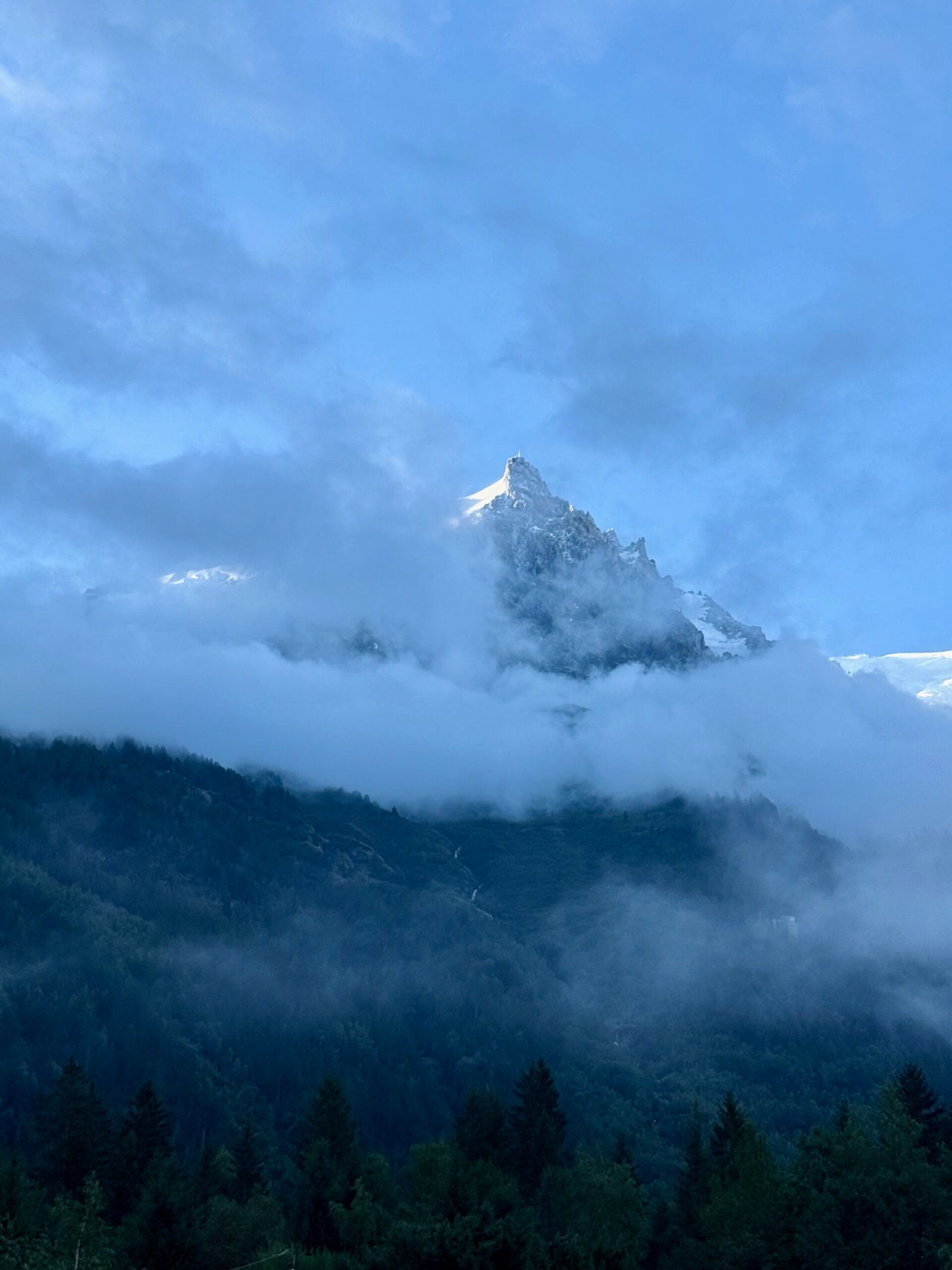 Aiguille du Midi summit peeking through morning clouds above Chamonix, France, as seen while walking to the cable car station.