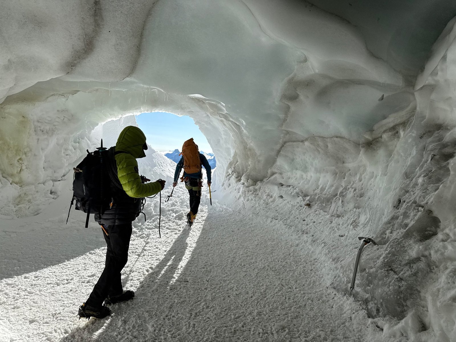 Hikers walking inside an ice-covered tunnel at the Aiguille du Midi summit station, descending toward the glacier below.