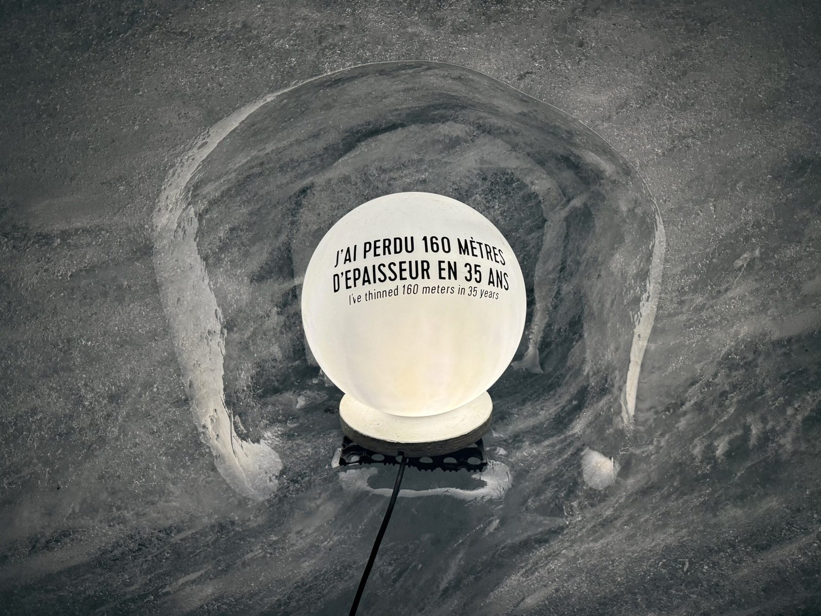 Illuminated globe-shaped lamp embedded in Grotte de Glace wall, displaying the message “I’ve thinned 160 meters in 35 years” in French and English.