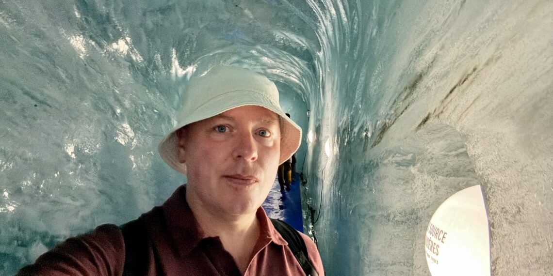 Don Trynor, author of Curious Don, inside the Grotte de Glace at Mer de Glace, surrounded by smooth blue glacier ice.