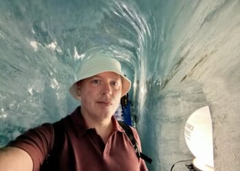 Don Trynor, author of Curious Don, inside the Grotte de Glace at Mer de Glace, surrounded by smooth blue glacier ice.