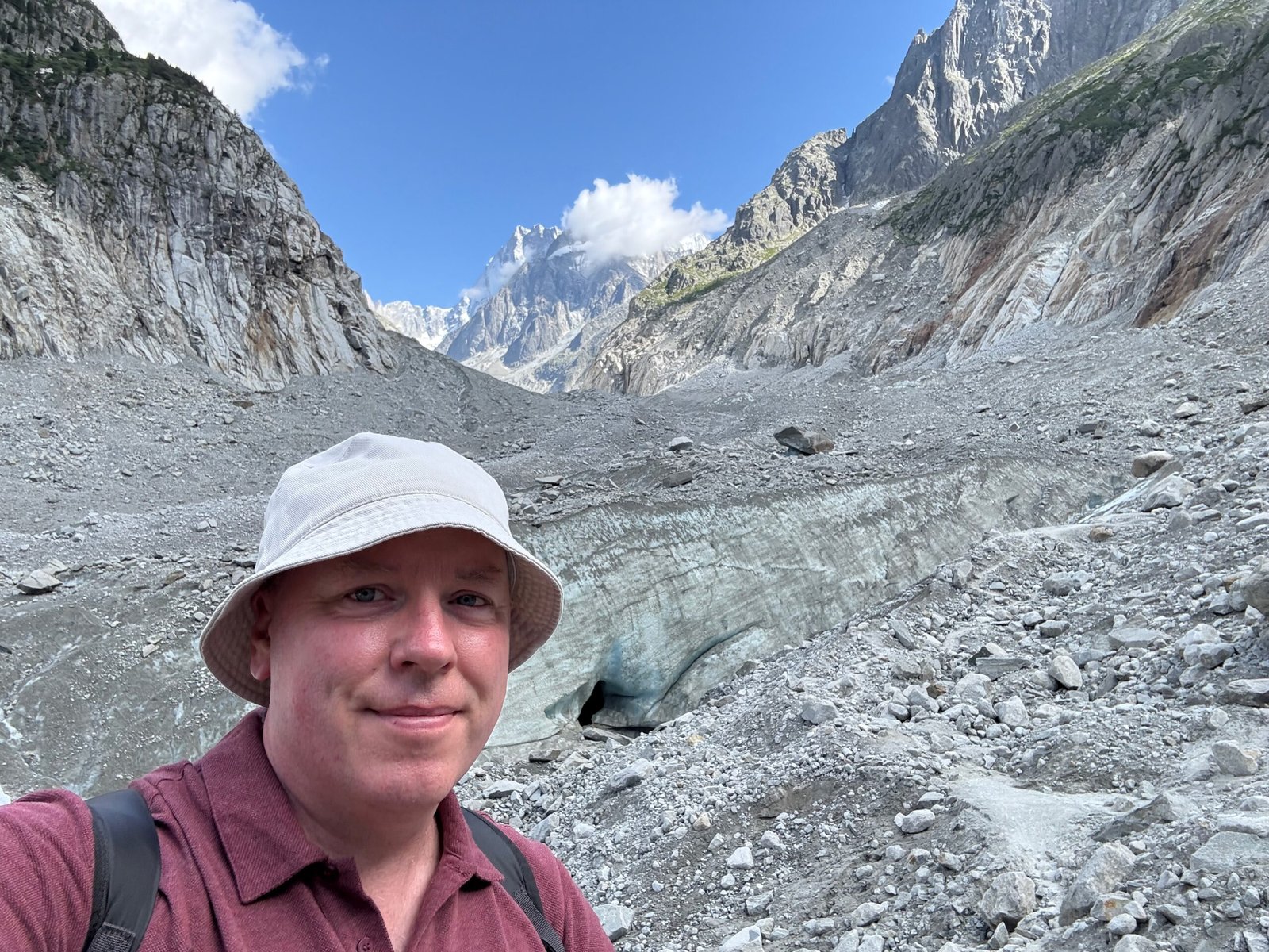 Don Trynor standing near the Mer de Glace glacier, with grey rock debris and towering alpine peaks in the background.