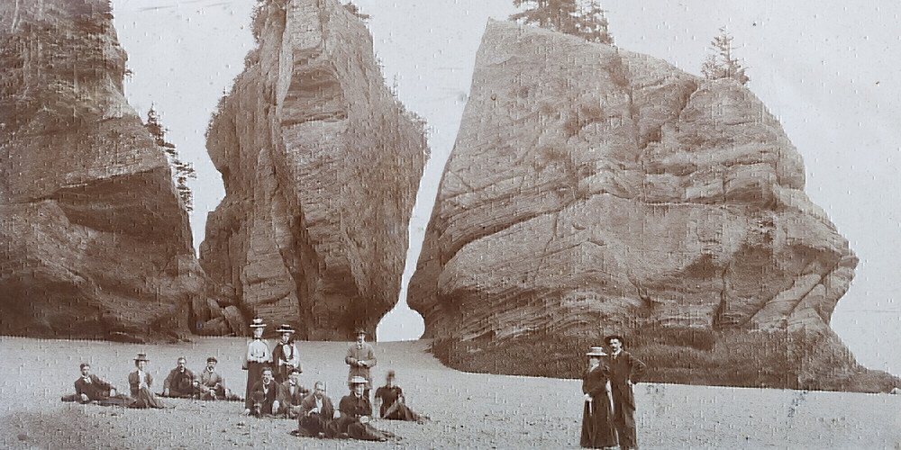 Historic photograph of visitors at the base of the Hopewell Rocks sea stacks in New Brunswick, taken at low tide in the early 1900s.
