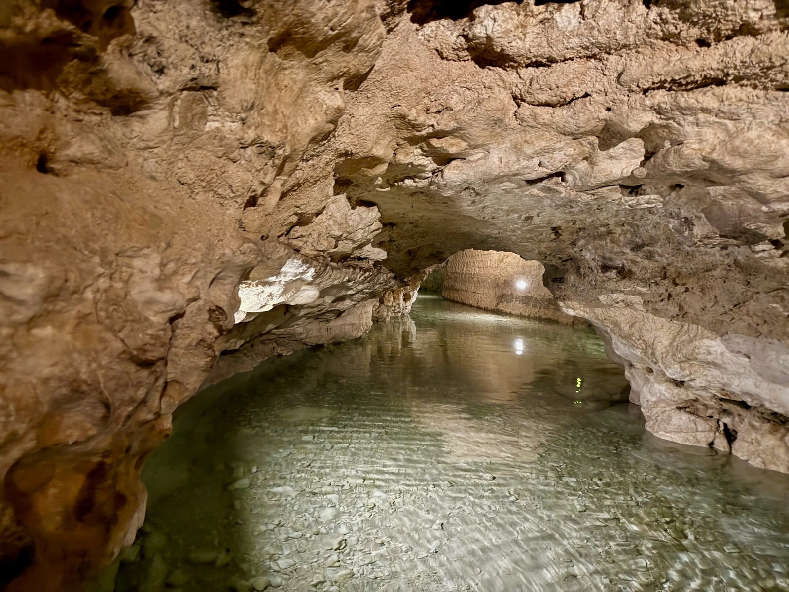 Winding tunnel of Tapolca Lake Cave with clear spring water and lights reflecting above and below the surface.