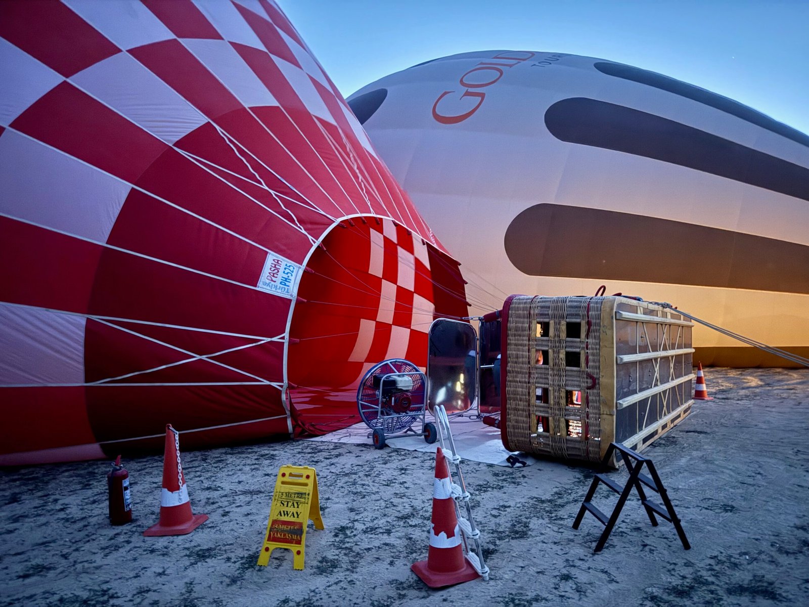 Ground crew inflating a Cappadocia hot air balloon at dawn with large fans and propane burners, preparing the basket and envelope for flight.
