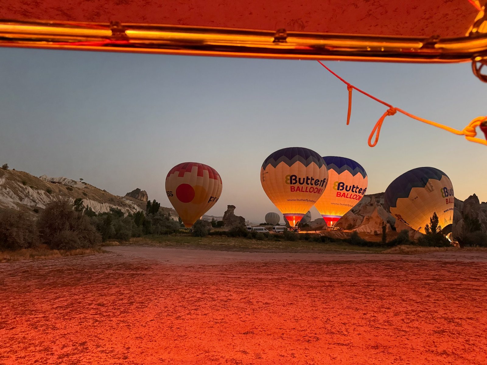 Cappadocia hot air balloons being inflated at dawn, with the orange glow from a nearby burner illuminating the ground in Türkiye’s volcanic valley.