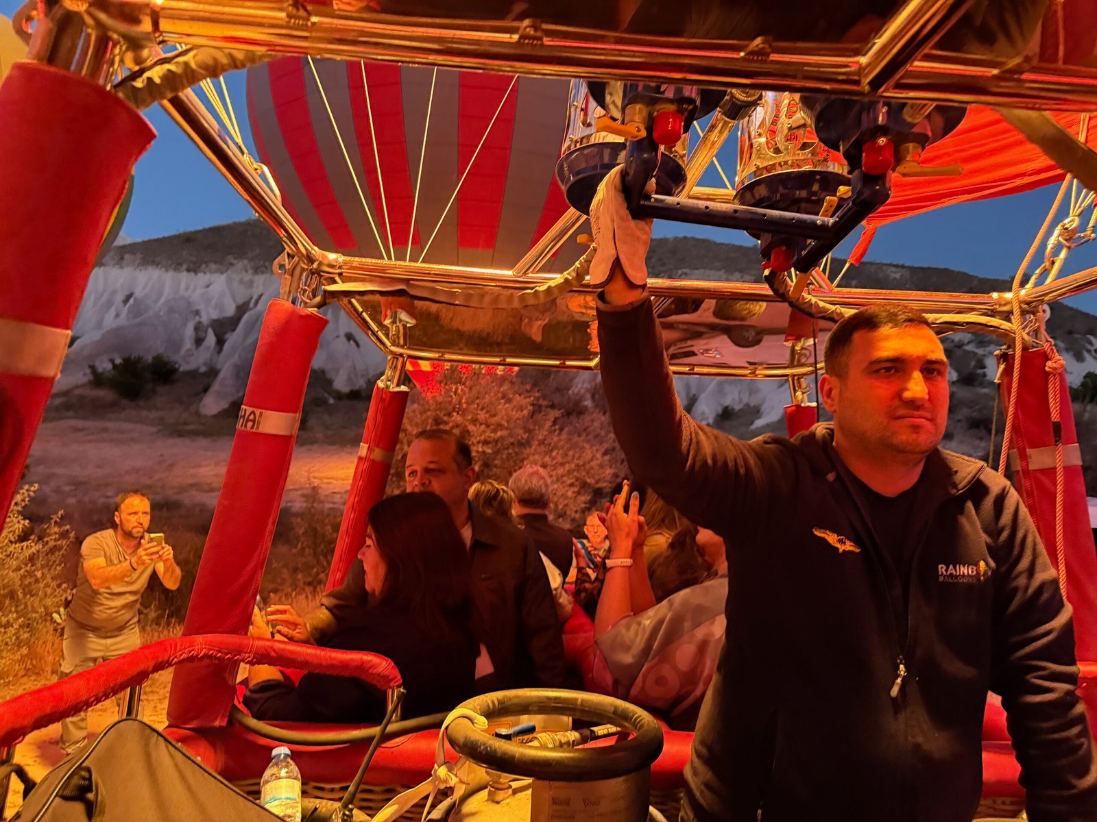 Cappadocia hot air balloon pilot activating the propane burner at dawn, with flames glowing orange across the basket and passengers before liftoff.