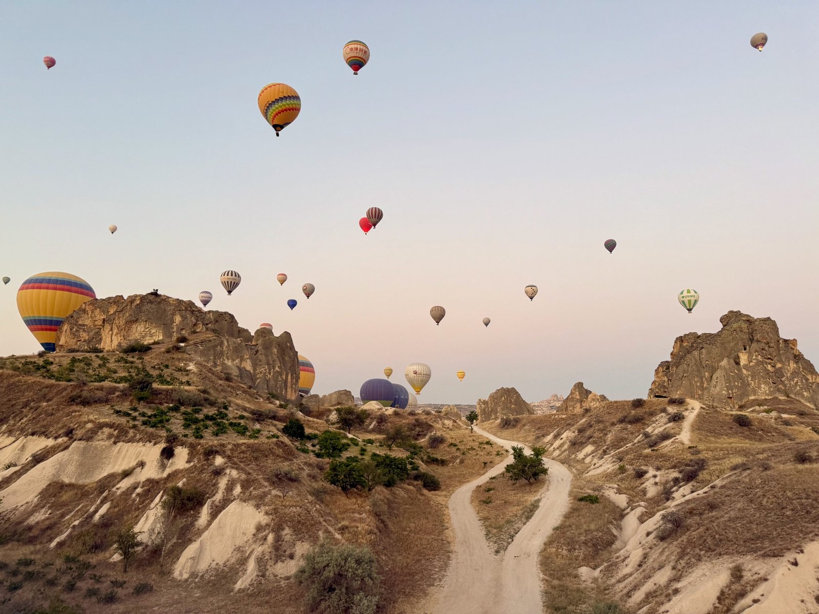 Low flight in a Cappadocia hot air balloon over rocky valleys and fairy chimneys with visible cave dwellings in Türkiye before sunrise.