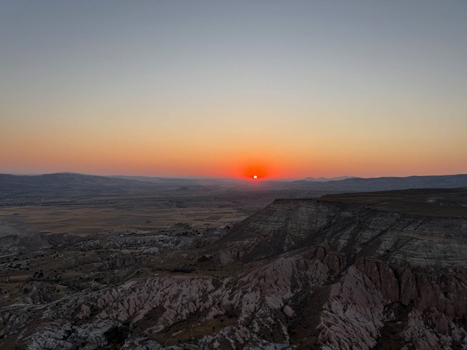 Sunrise seen from a Cappadocia hot air balloon, with volcanic cliffs and valleys below glowing in the warm colours of dawn.