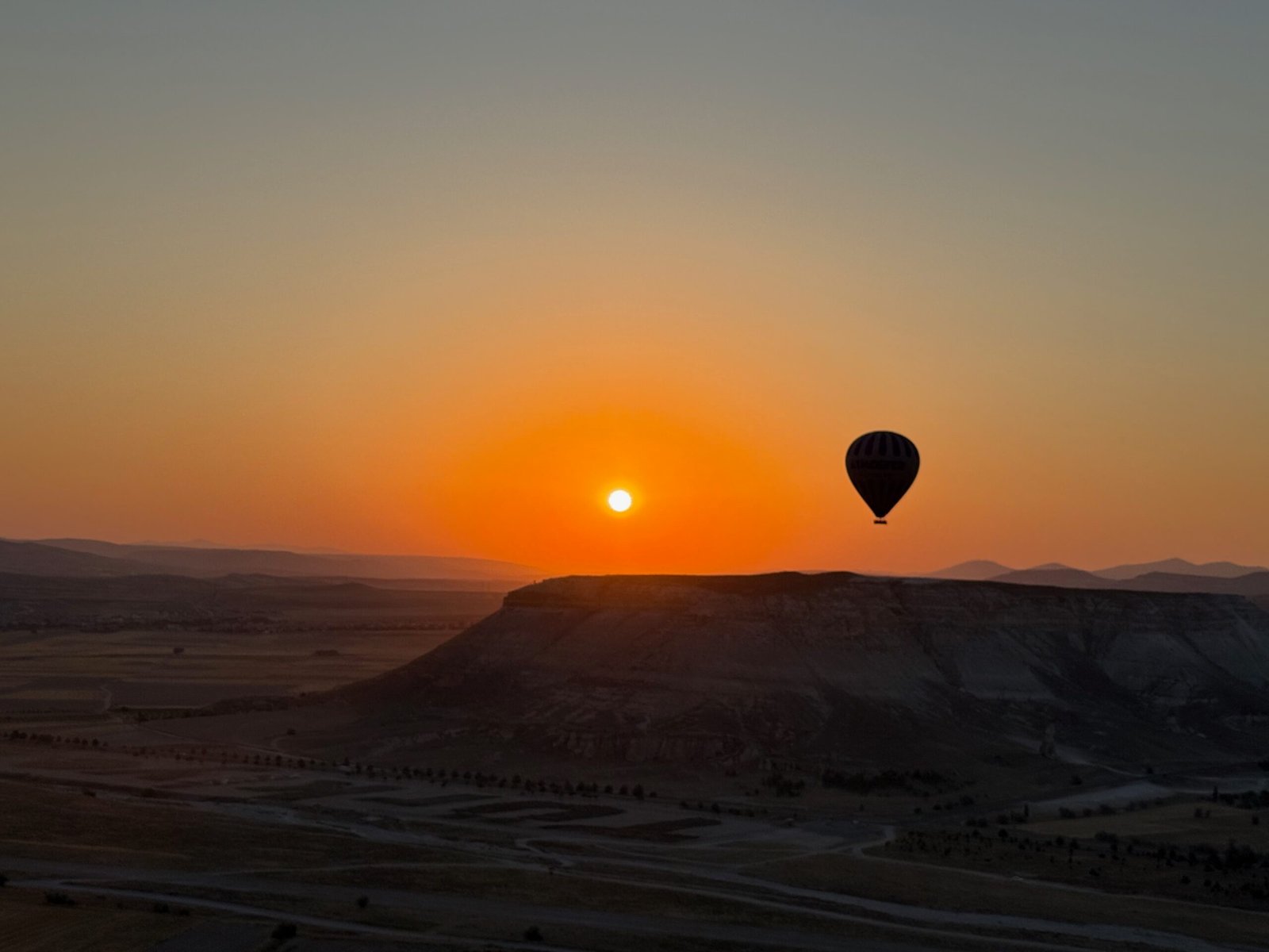 Silhouette of a Cappadocia hot air balloon at sunrise with the sun glowing above volcanic cliffs and valleys in Türkiye.