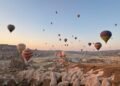 Cappadocia hot air balloon ride at sunrise with dozens of colorful balloons floating above the rocky valleys and fairy chimneys of Türkiye.