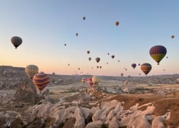 Cappadocia hot air balloon ride at sunrise with dozens of colorful balloons floating above the rocky valleys and fairy chimneys of Türkiye.