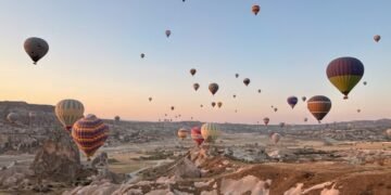Cappadocia hot air balloon ride at sunrise with dozens of colorful balloons floating above the rocky valleys and fairy chimneys of Türkiye.