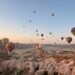 Cappadocia hot air balloon ride at sunrise with dozens of colorful balloons floating above the rocky valleys and fairy chimneys of Türkiye.